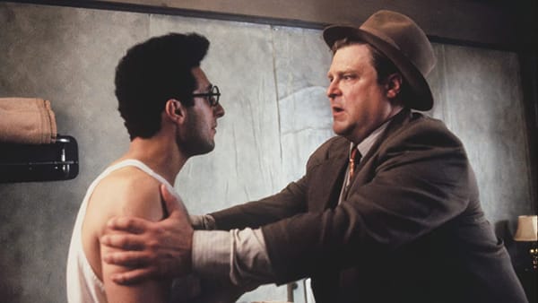 Barton Fink: Hotel room. Wallpaper peeling. Charlie Meadows holds Barton Fink by the arms, a look of desperation on his face.